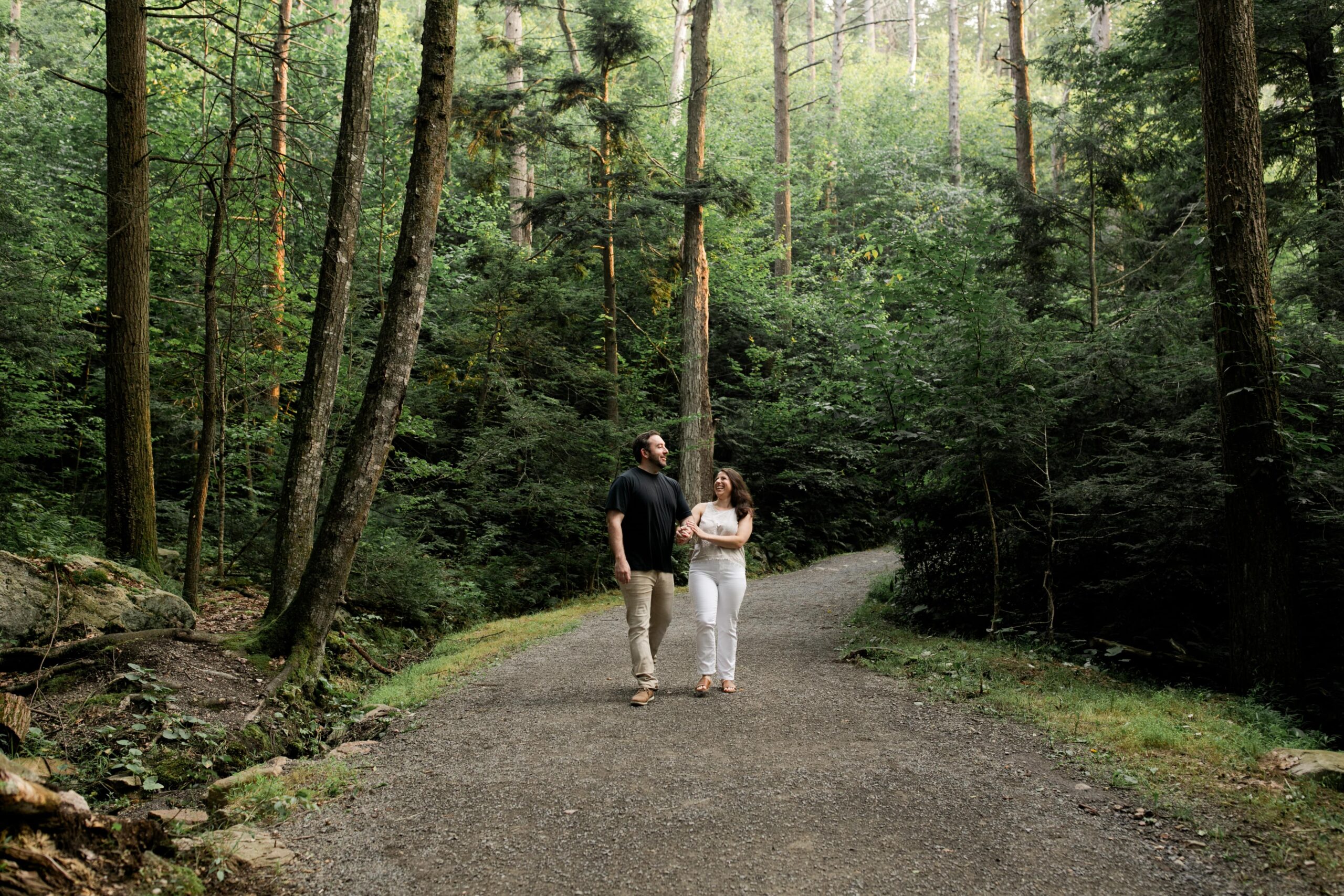 Bride and groom stroll through a shady forest during their New York adventure engagement session. 