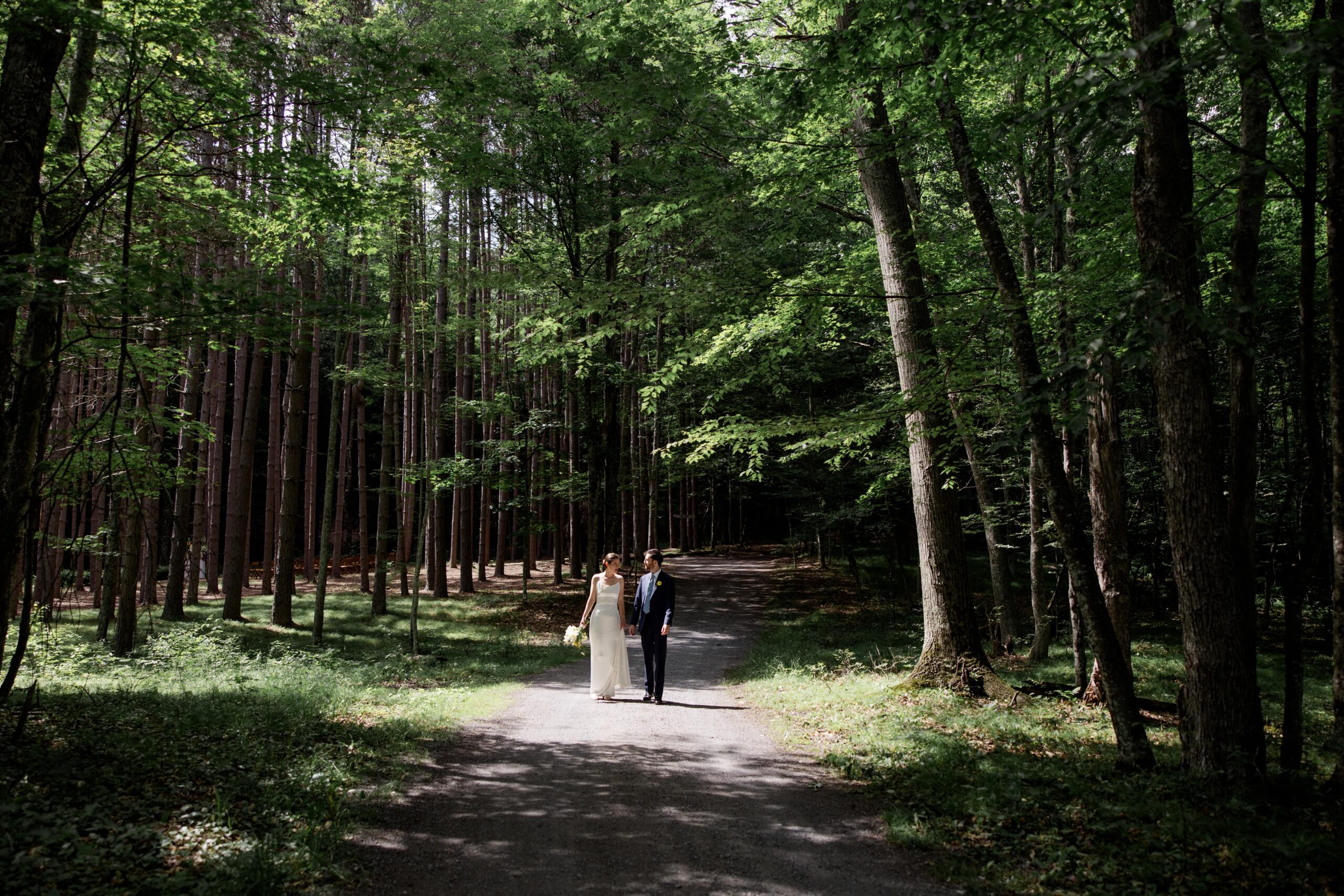 Bride and groom walk a shady forest path at Roxbury Barn & Estate wedding venue. 