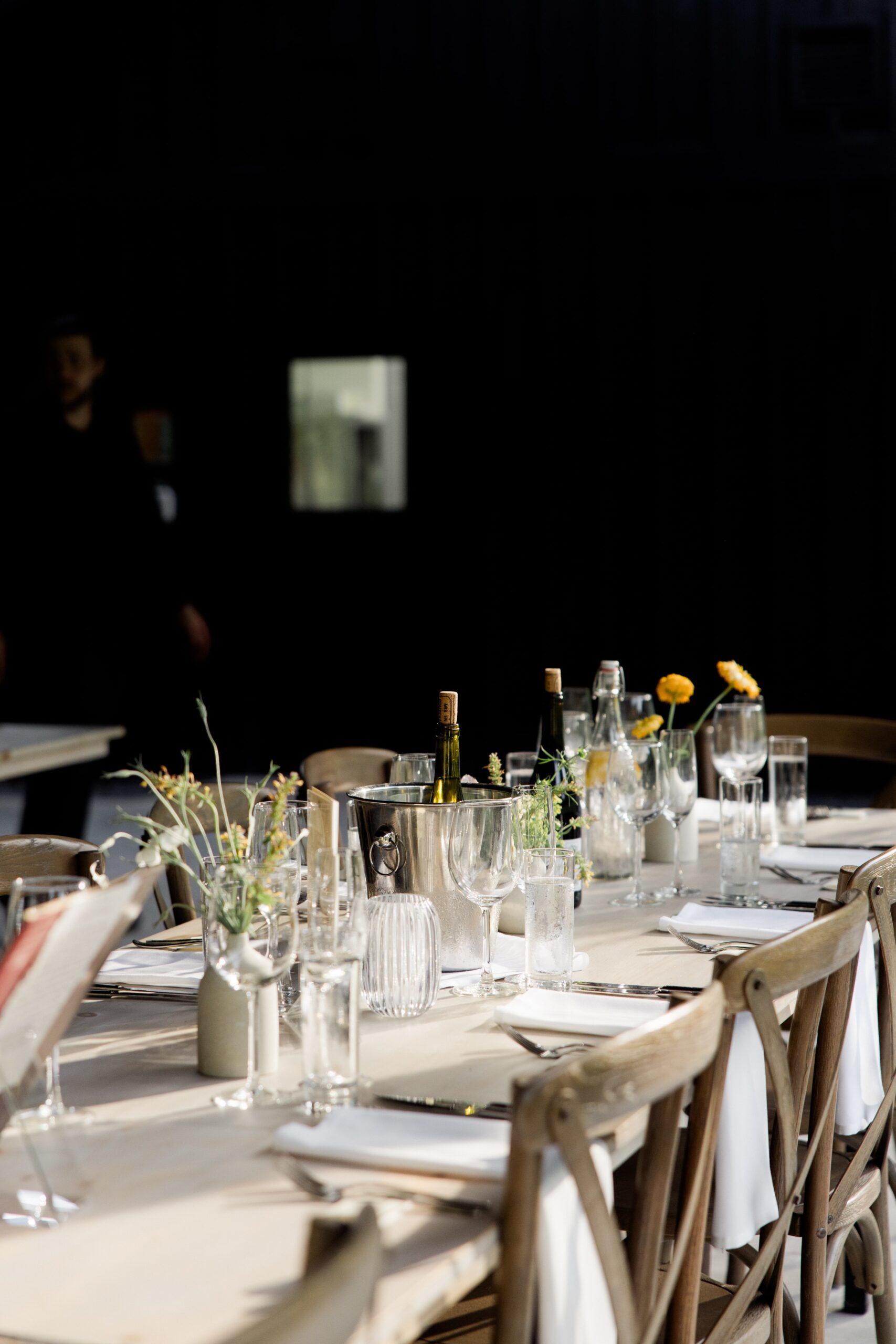 Beige tablecloth and wood chairs line an indoor/outdoor wedding reception table at a barn wedding venue in upstate NY. 