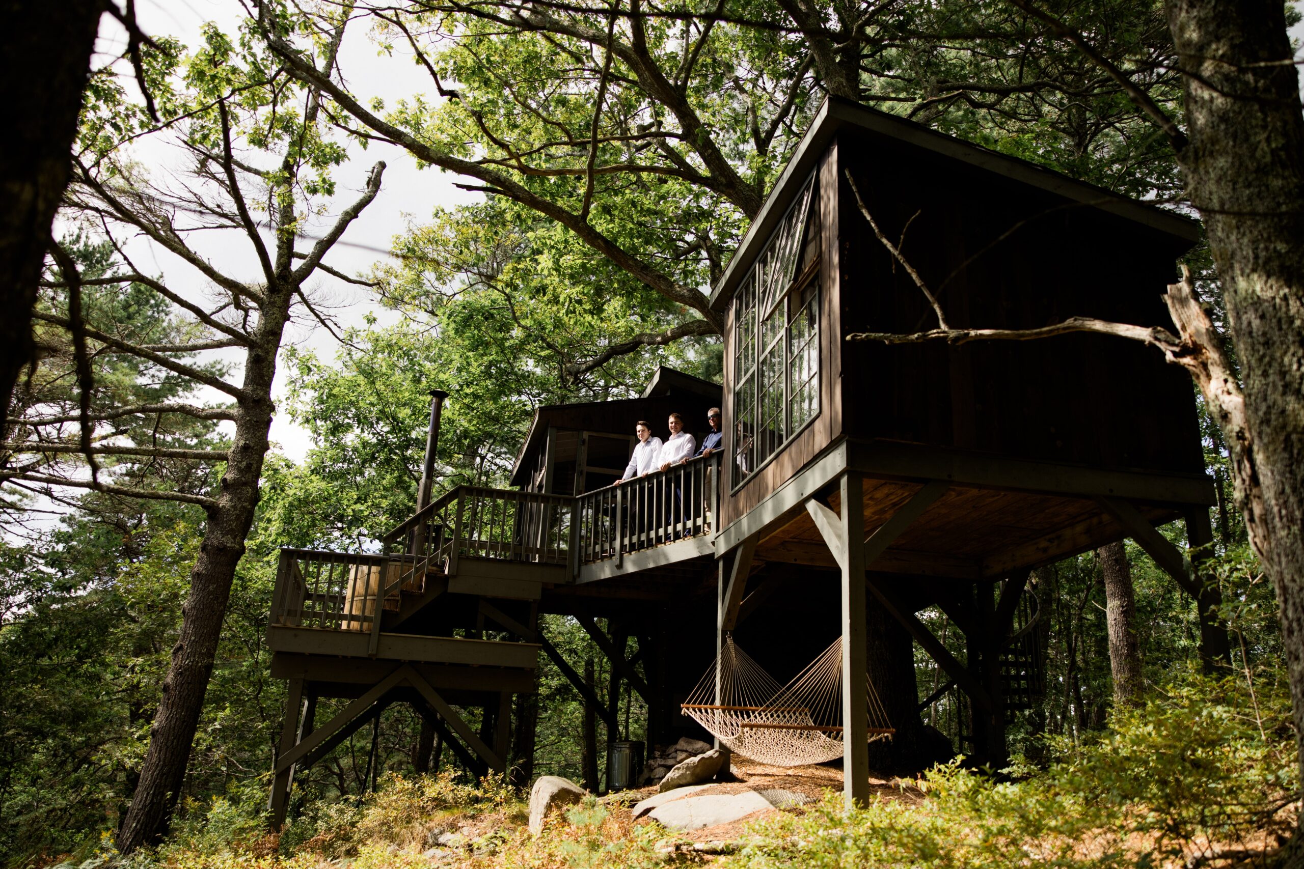 Groom and guests stand on the deck of a treehouse cabin in Maine. 