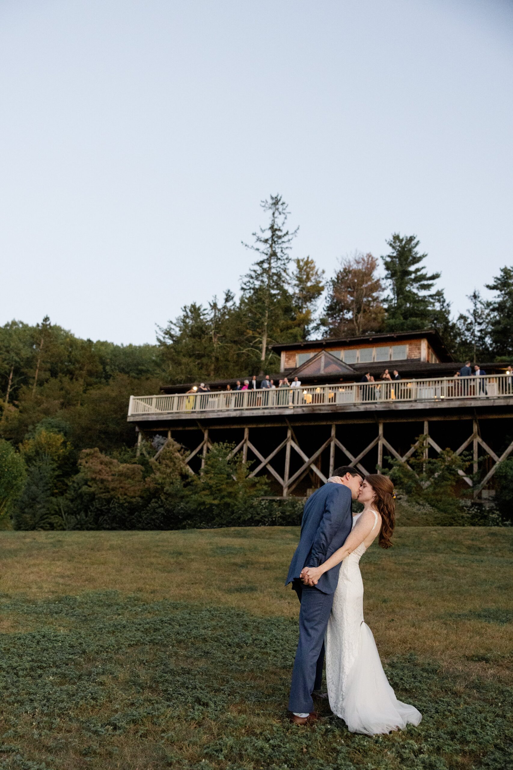 Bride and groom kiss while family looks on from the patio of their shared house during their small, intimate wedding celebration. 