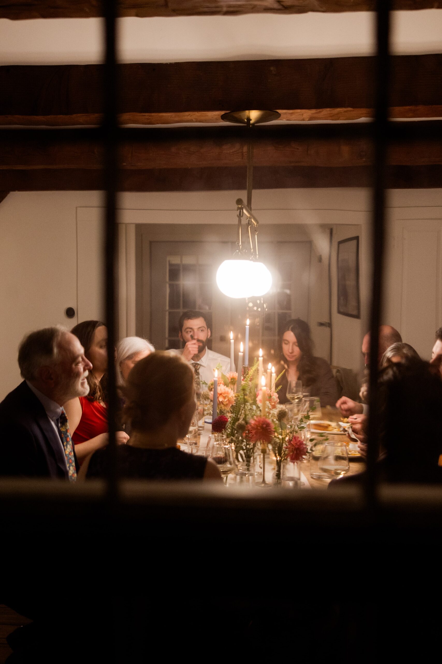 Guest sit around a dinner table and enjoy a catered dinner from a private chef during an elopement celebration. 