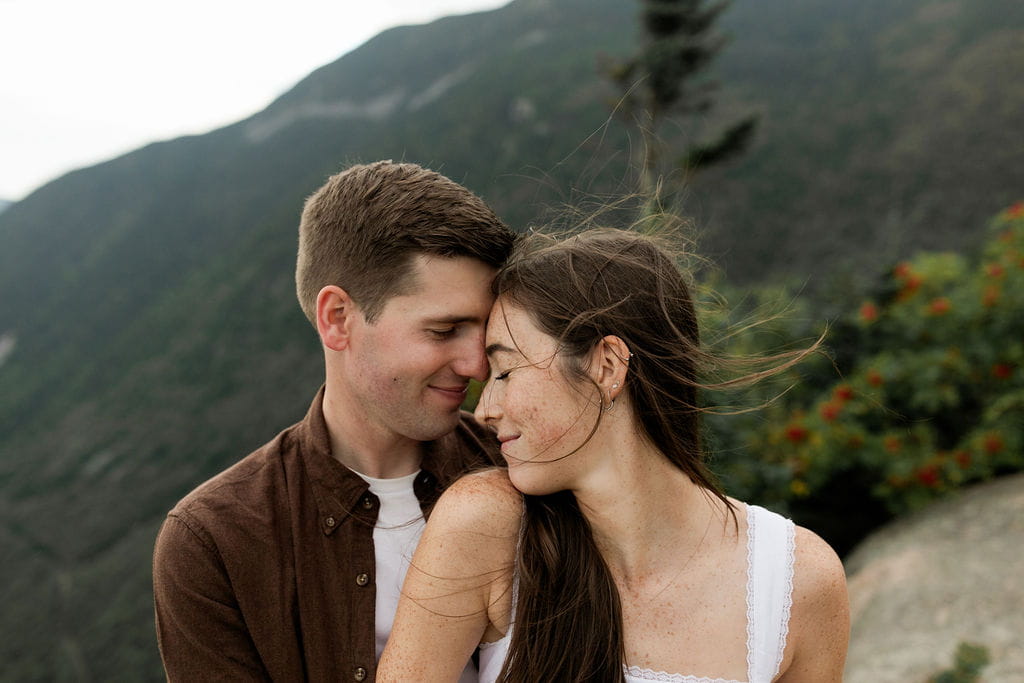 Man and woman lean their foreheads against each other during their adventure engagement photos in New England.