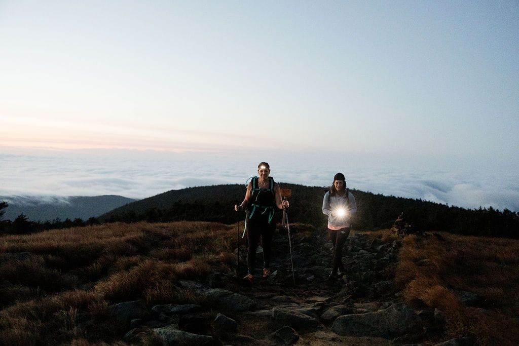 Two women hike with headlamps during their sunrise adventure session in the White Mountains.