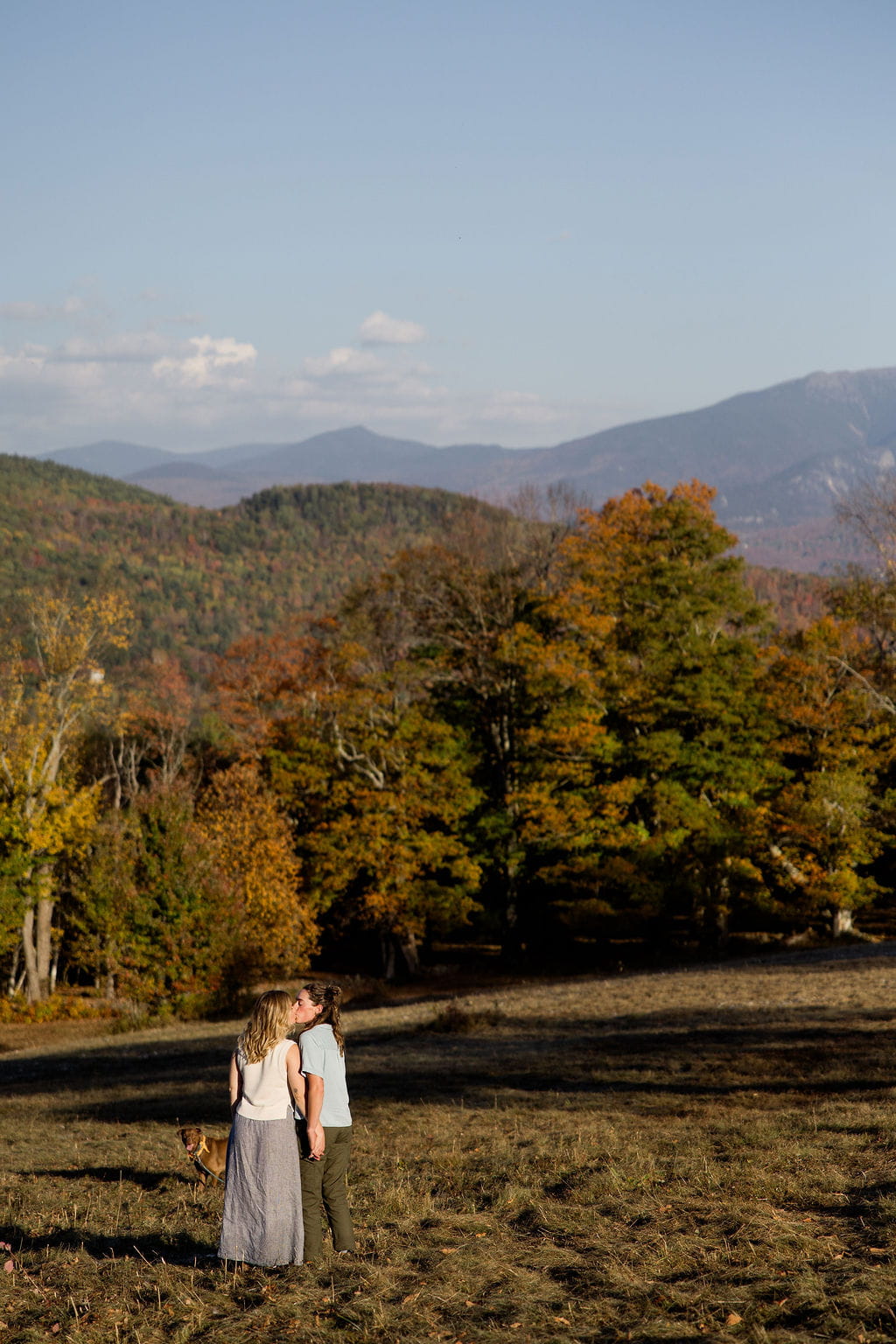 Two women hold hands and kiss in a sprawling field during their adventure session.