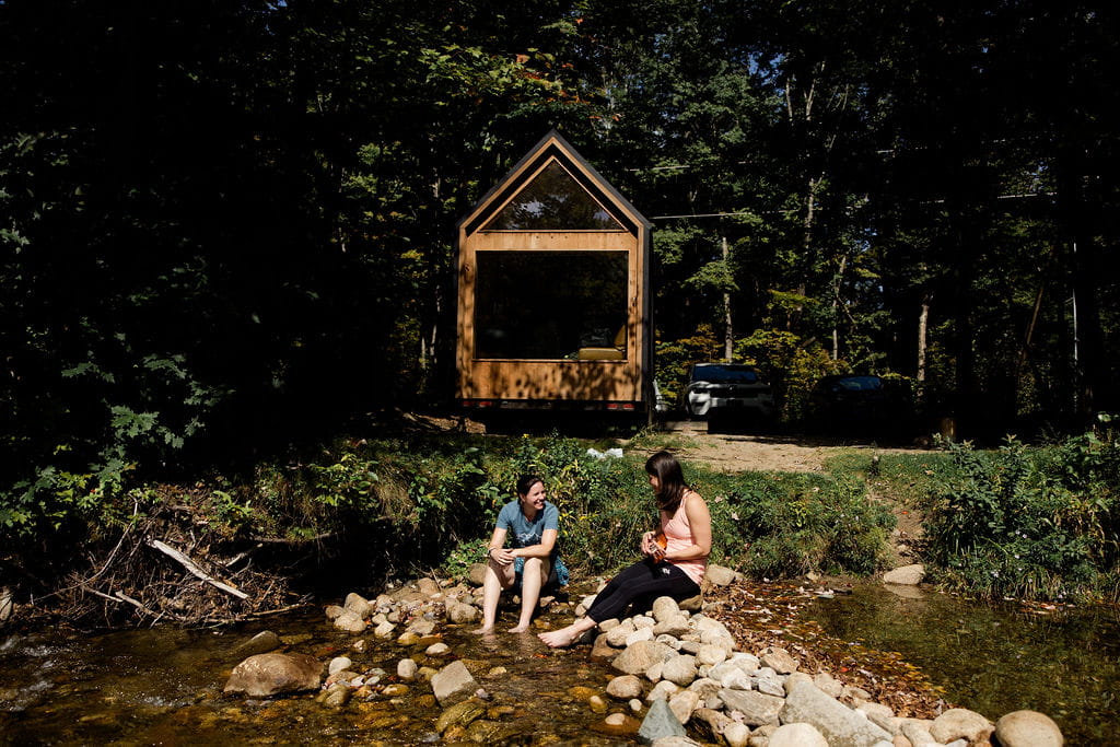 Two women sit on rocks next to a riverbank during their couples session in the White Mountains.